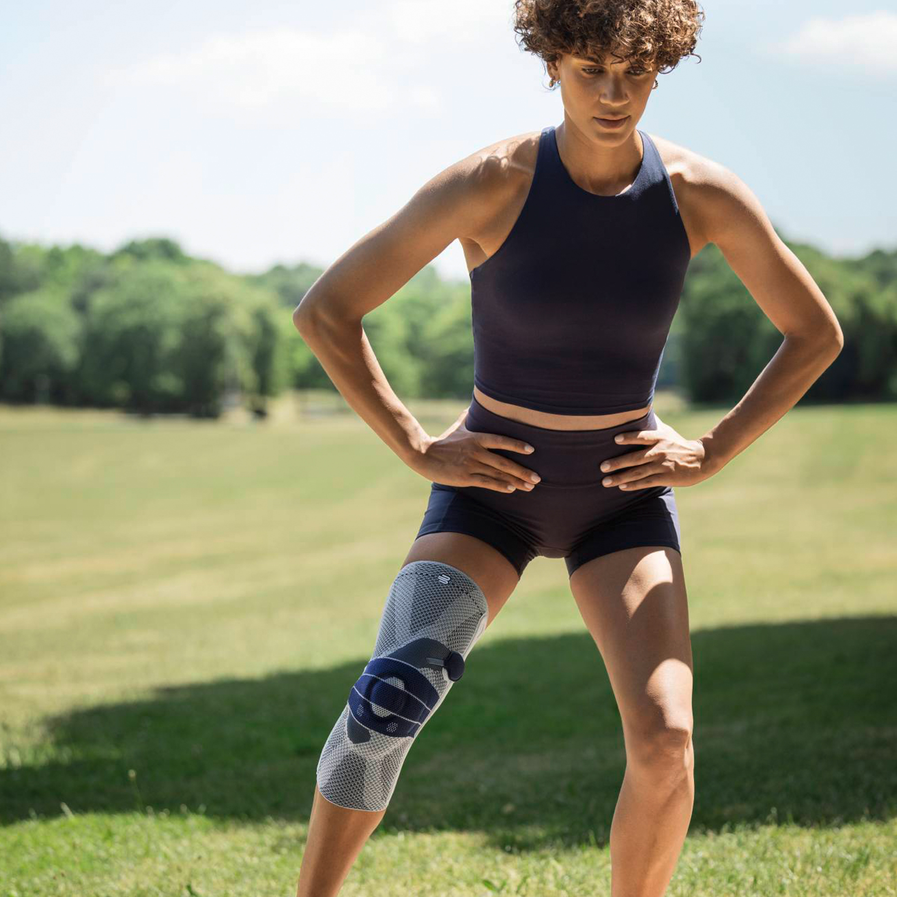 Atleet warmt buiten op met kniebrace voor stabiliteit tijdens training op gras.