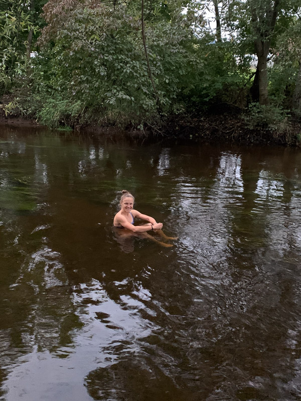 Anna Hahner in de rivier, omringd door bomen, glimlachend en naar de camera kijkend.