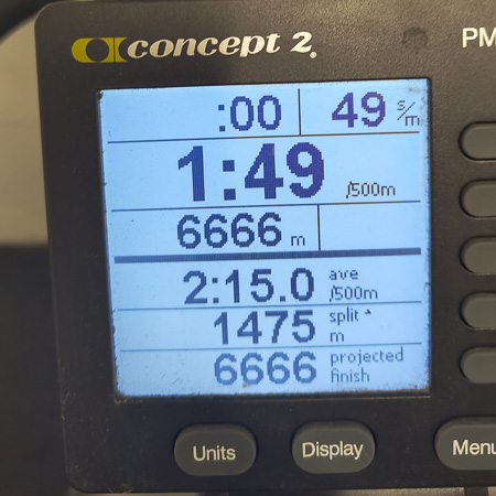 Close-up van een SkiErg-trainingsmonitor. Het scherm toont een afstand van 6666 meter, een gemiddelde tijd van 2:15 per 500 meter en een tijd van 1:49 per 500 meter.