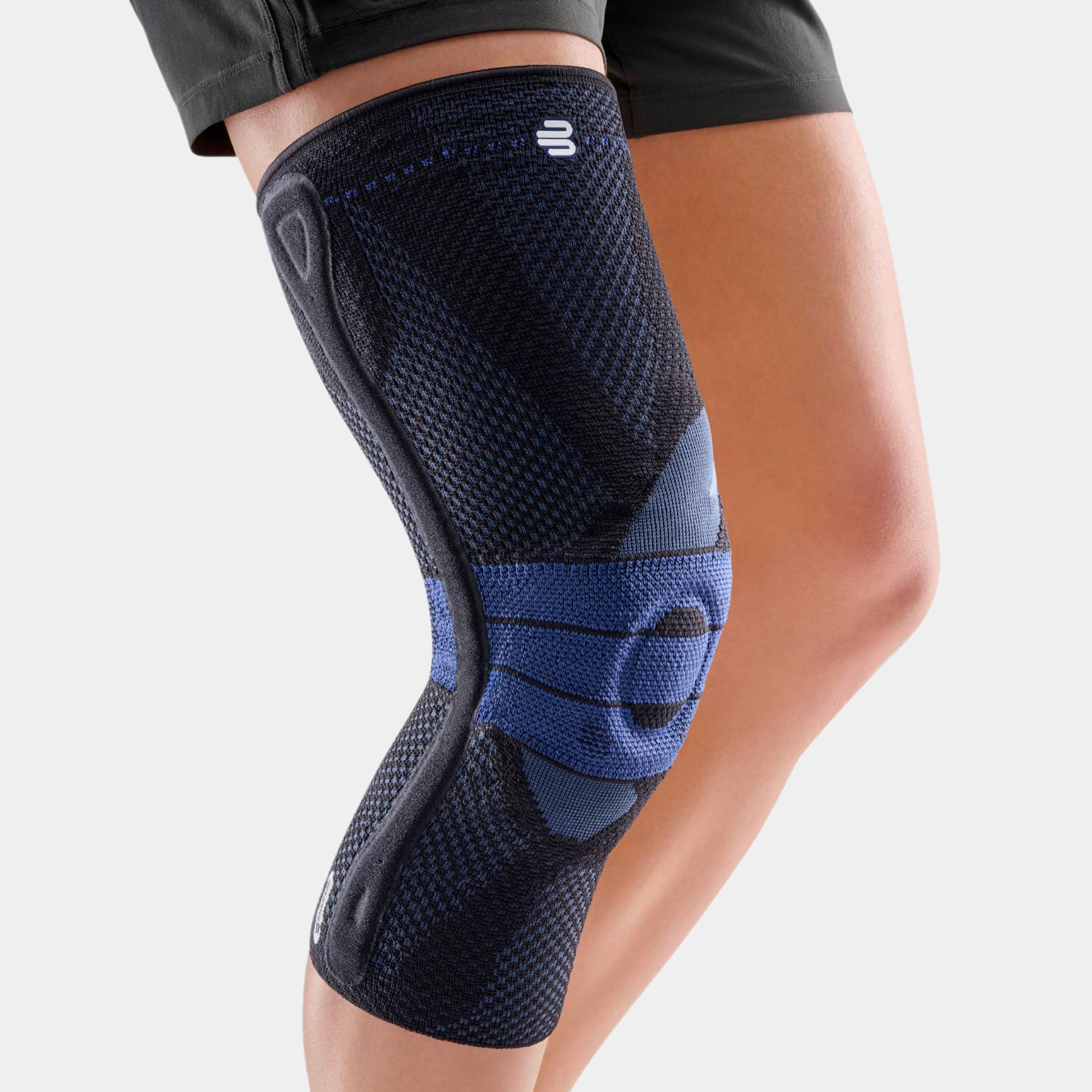 Zwarte GenuTrain P3 kniebrace op het been met zijstabilisator en compressiebreisel.
