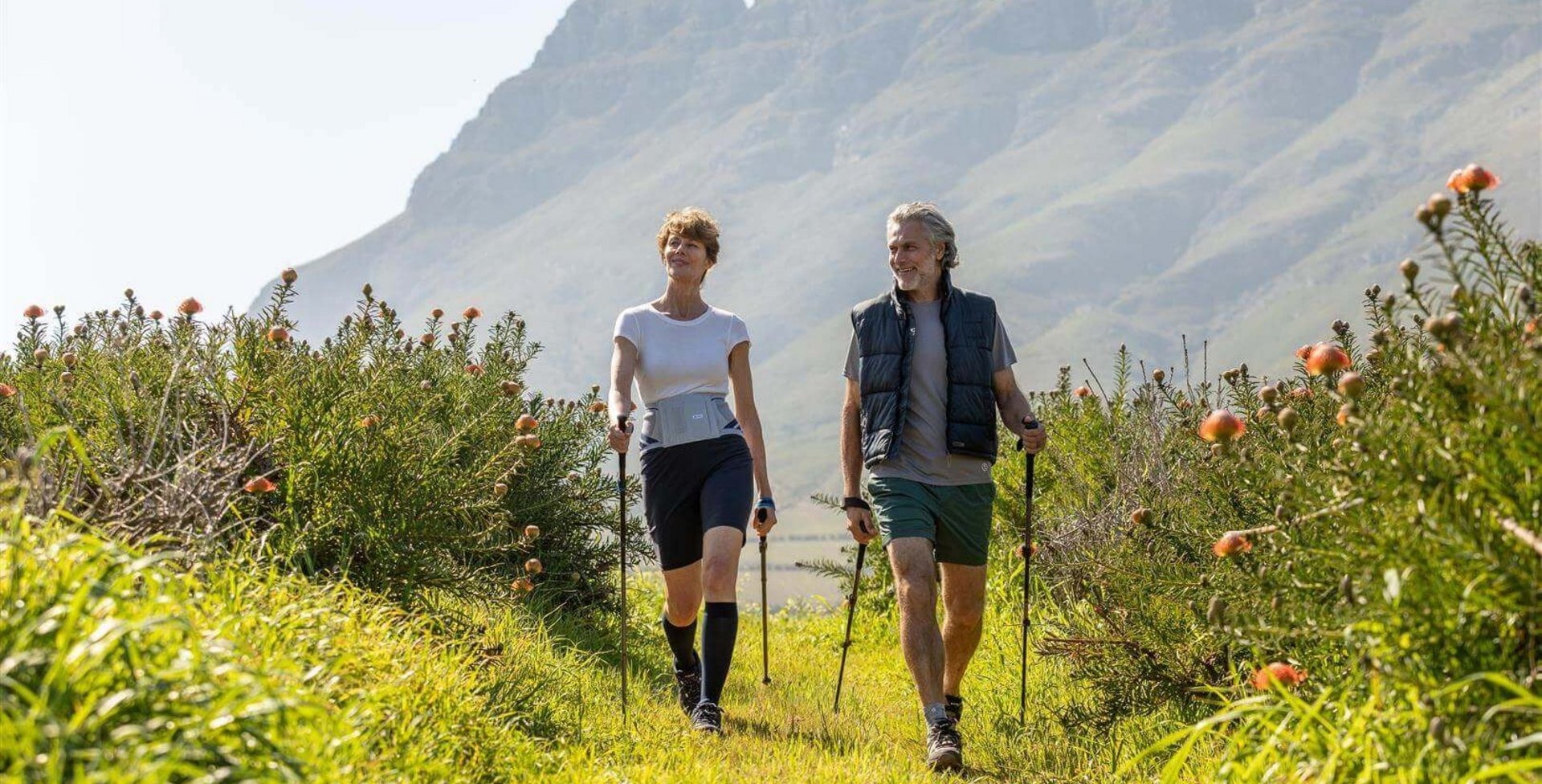 Op het beeld zie je hoe een ouder stel in de natuur aan nordic walking doet. Ze dragen Train-bandages van Bauerfeind om hun gewrichten en rug tijdens het bewegen te ontlasten.