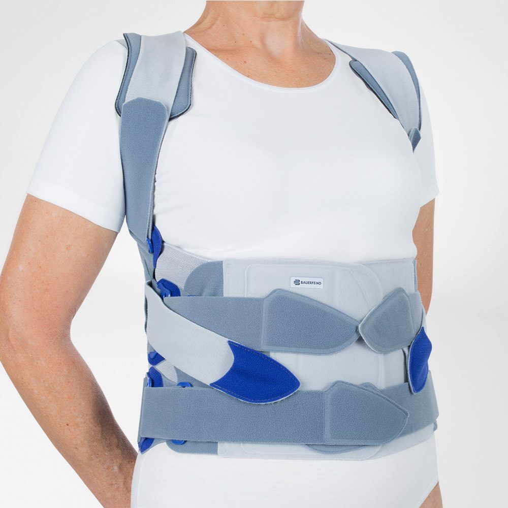Persoon in wit shirt draagt een grijs-blauw rugkorset met schouderbanden en verstelbare sluitingen.