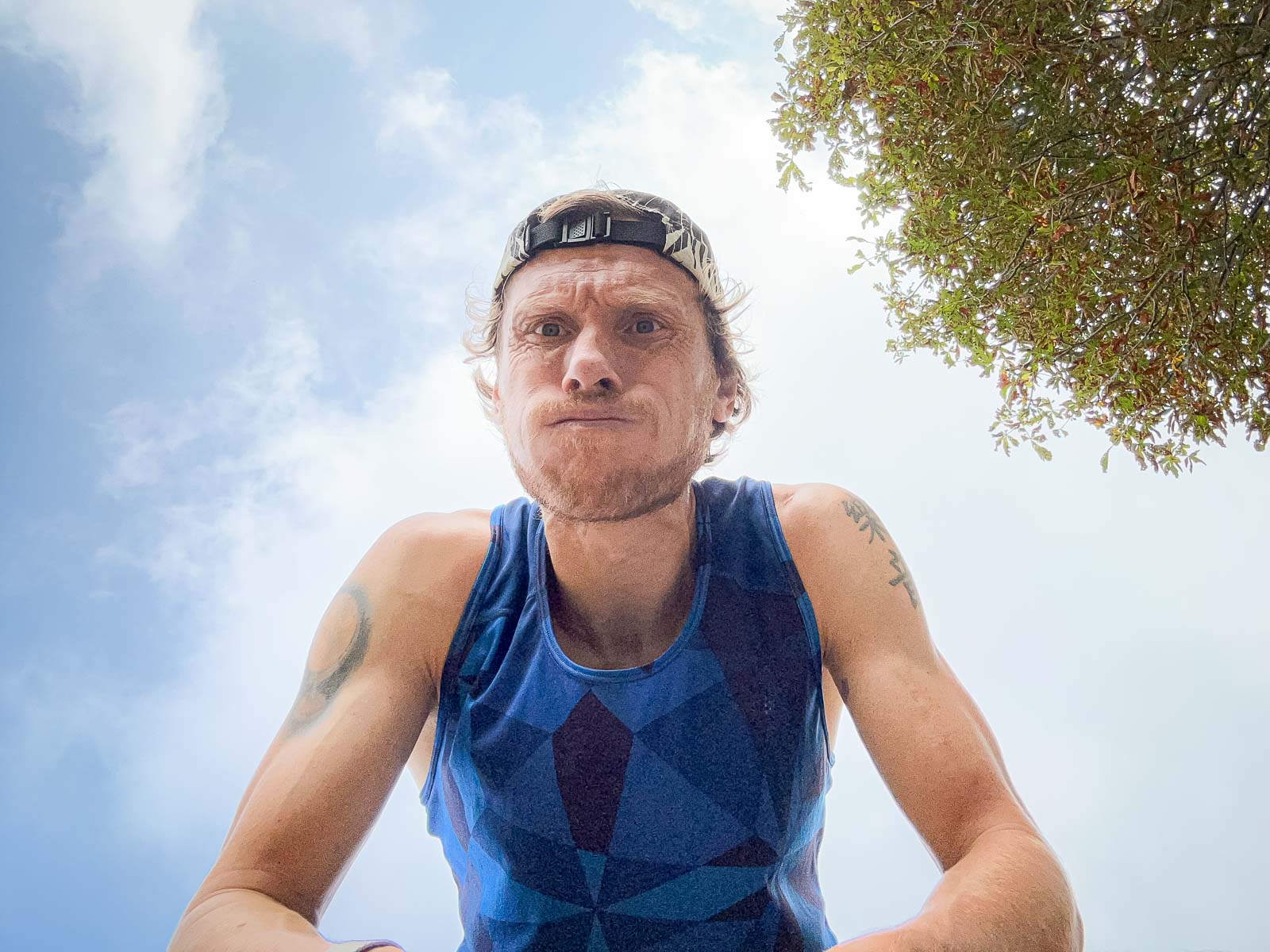 Close-up van een loper die zwaar ademt na een run. Hij draagt een blauw shirt en een pet, terwijl hij in de camera kijkt.