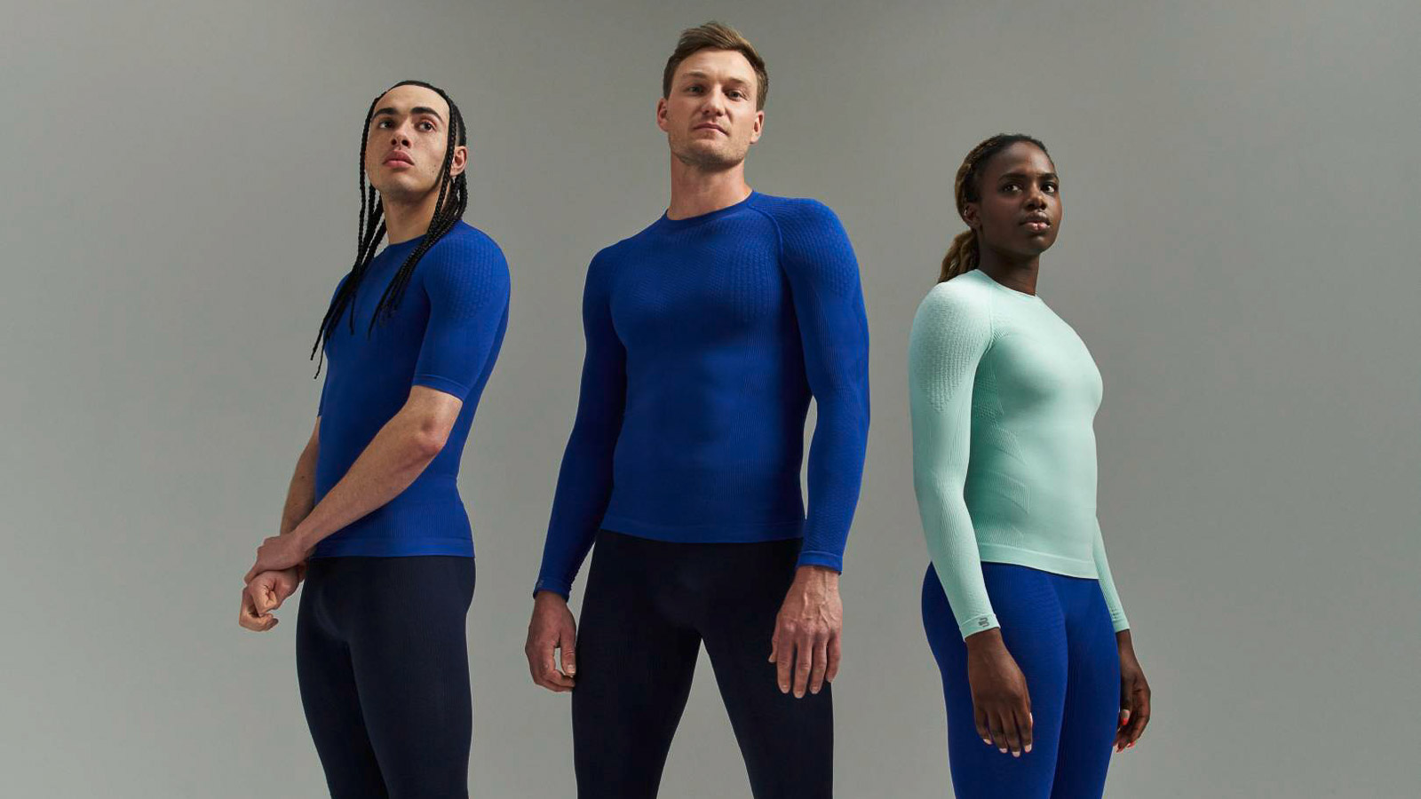 Drie atleten in sportkleding met compressieshirts en compressiebroeken voor een grijze achtergrond.