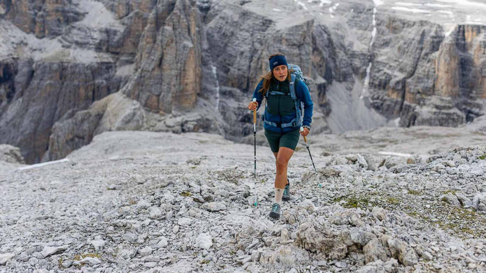 Een wandelaar in de Dolomieten loopt met stokken over een steenveld en draagt een wandelbandage. Italienisch: Una escursion