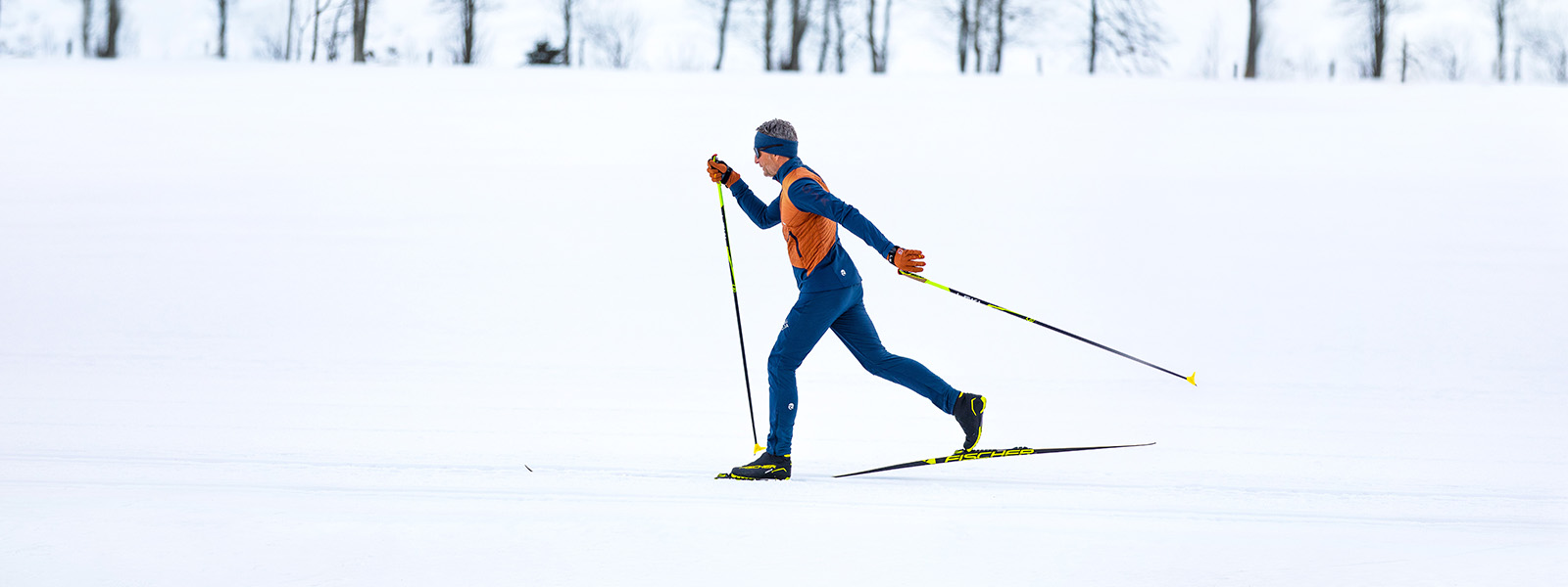 Een man in oranje en blauwe kleding langlauft door de sneeuw.