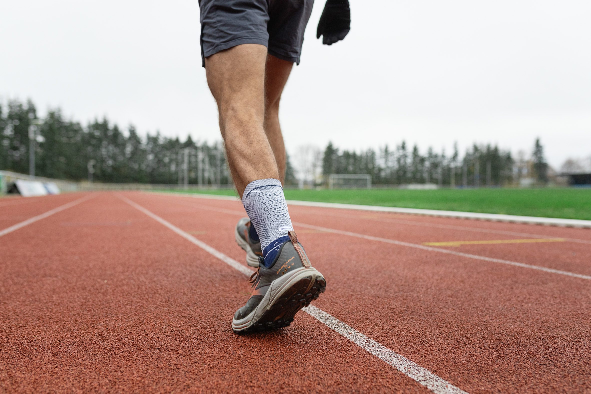 Hardloper op een rode atletiekbaan, close-up van benen en schoenen tijdens het rennen.