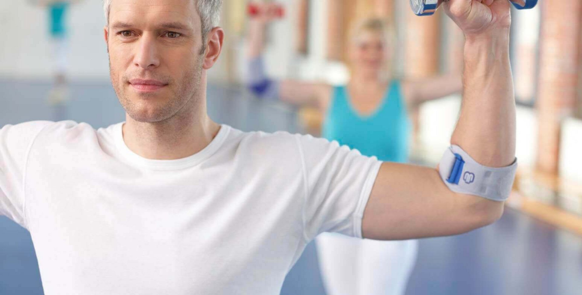 Een man traint zijn onderarm met een dumbbell. Daarbij draagt hij een EpiTrain bandage om zijn elleboog, die stabilisatie en ontlasting biedt.