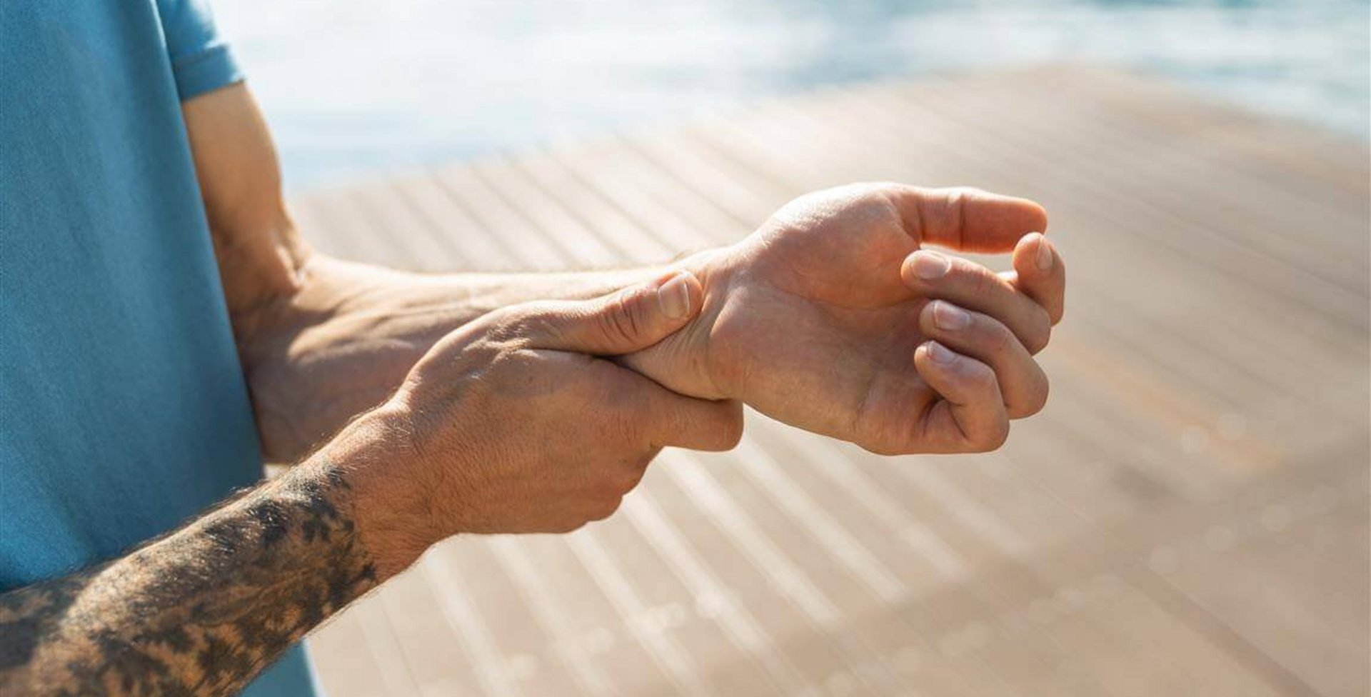 Beelduitsnede van een man met tatoeages die naar zijn pijnlijke pols grijpt. Lees hoe Bauerfeind je helpt bij polsklachten.