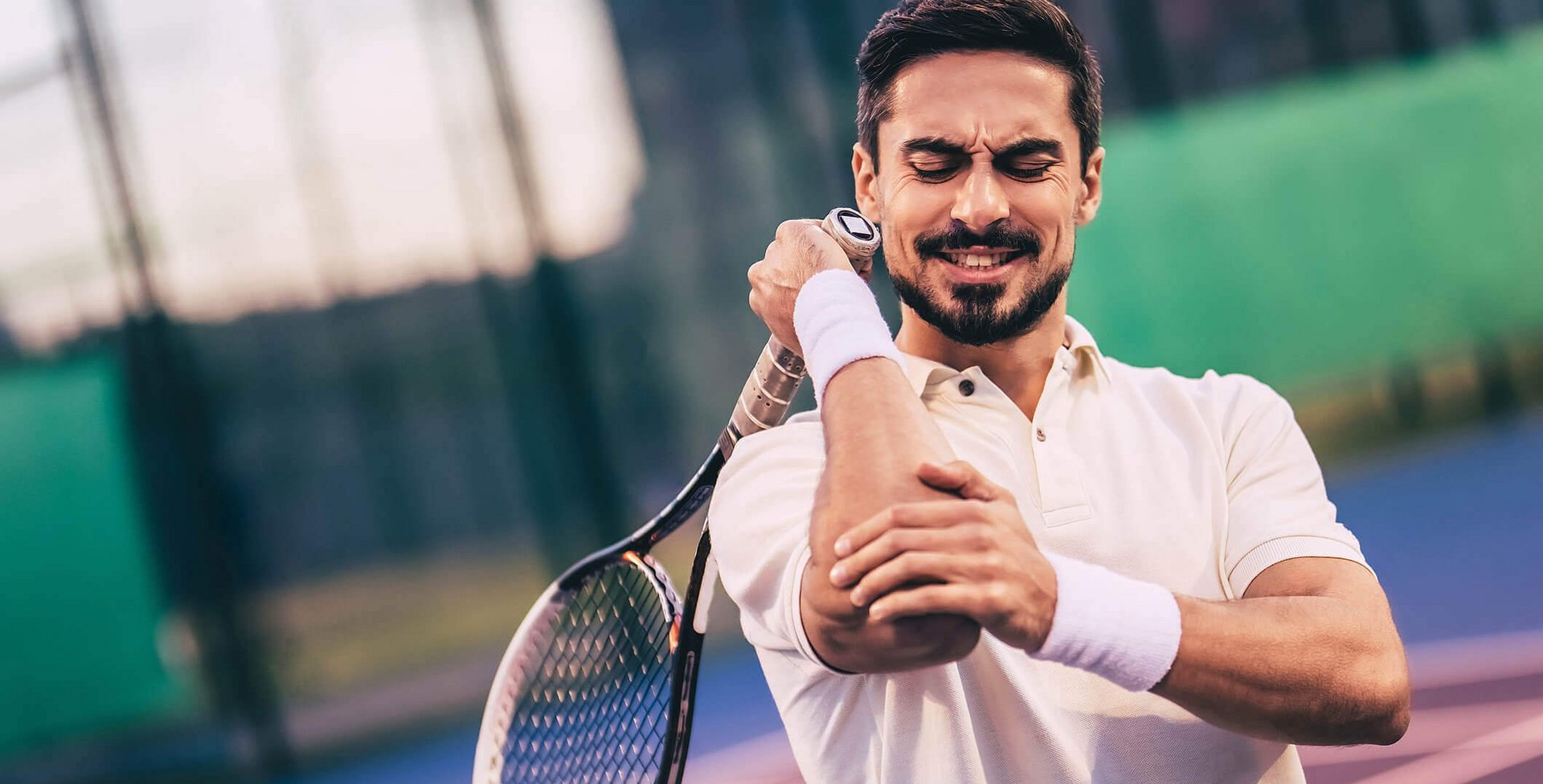 De foto toont een tennisser met elleboogpijn. Bij dit soort klachten in de sport of het dagelijks leven is het belangrijk om de oorzaak te achterhalen.