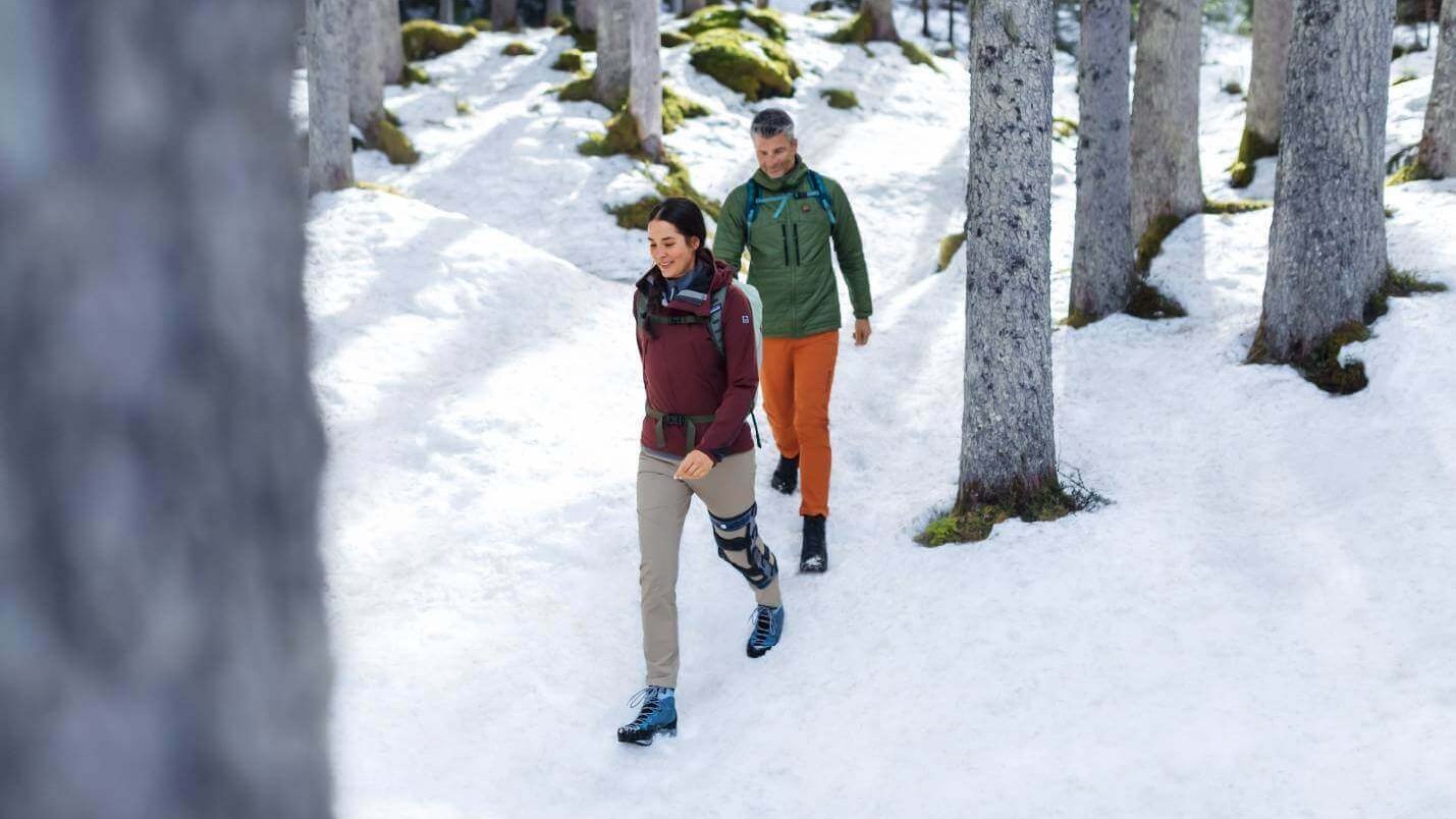 Op de foto zijn twee personen tijdens een winterwandeling te zien. Een van de personen draagt de knieorthese SecuTec Genu van Bauerfeind.