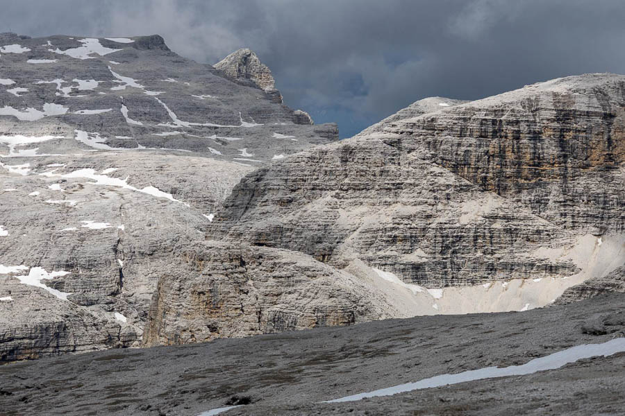 Een rotsachtig landschap in de Dolomieten met verspreide sneeuwplekken en een bewolkte hemel.