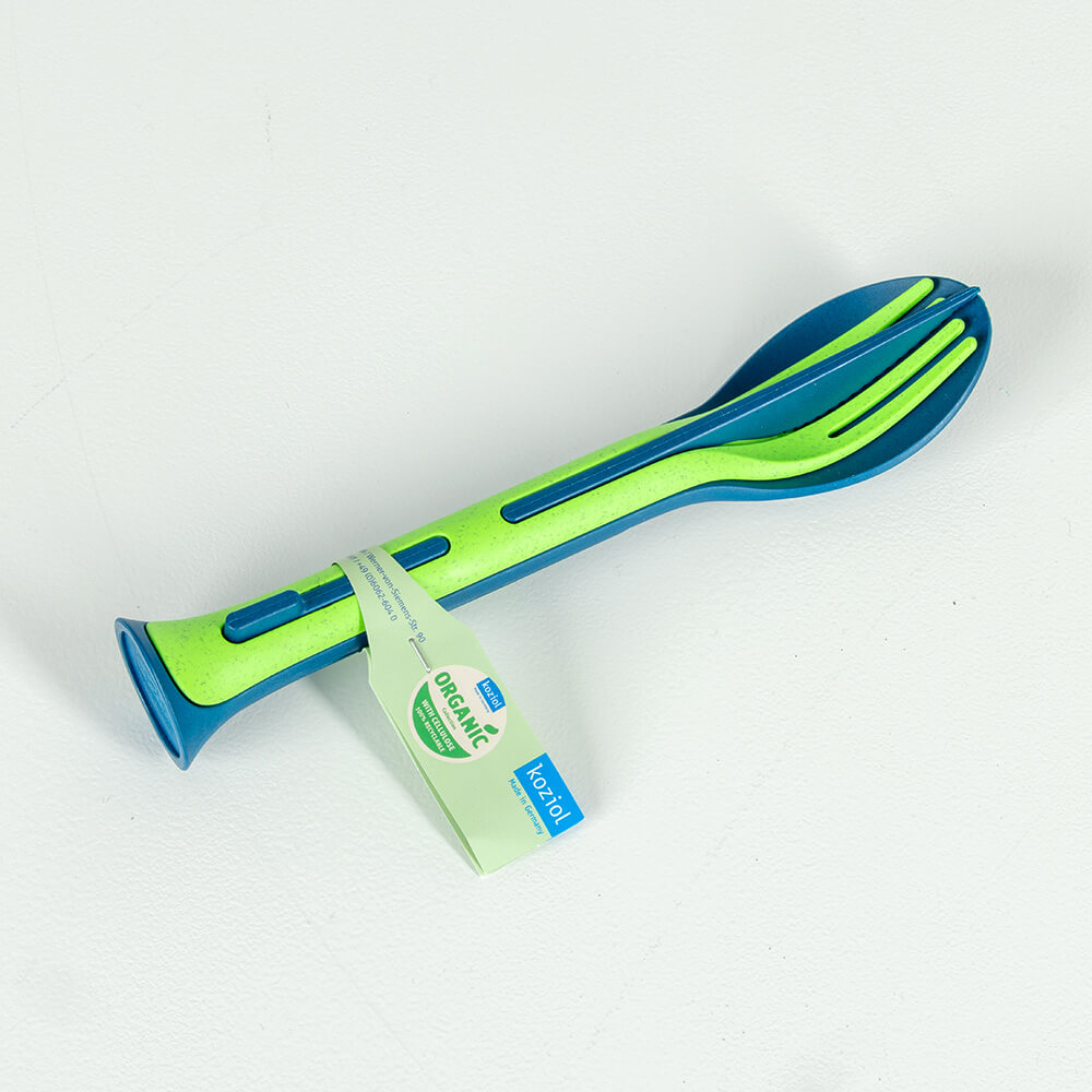 Het Koziol KLIKK bestekset in blauw en groen, bestaande uit een lepel, vork en mes, compact bij elkaar gevoegd. Gemaakt van organisch materiaal, ideaal voor onderweg en milieuvriendelijk.