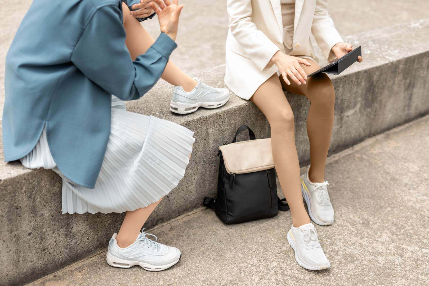Twee vrouwen zitten op een stenen muurtje. De focus ligt op hun benen, want ze dragen VenoTrain micro compressiekousen van Bauerfeind.