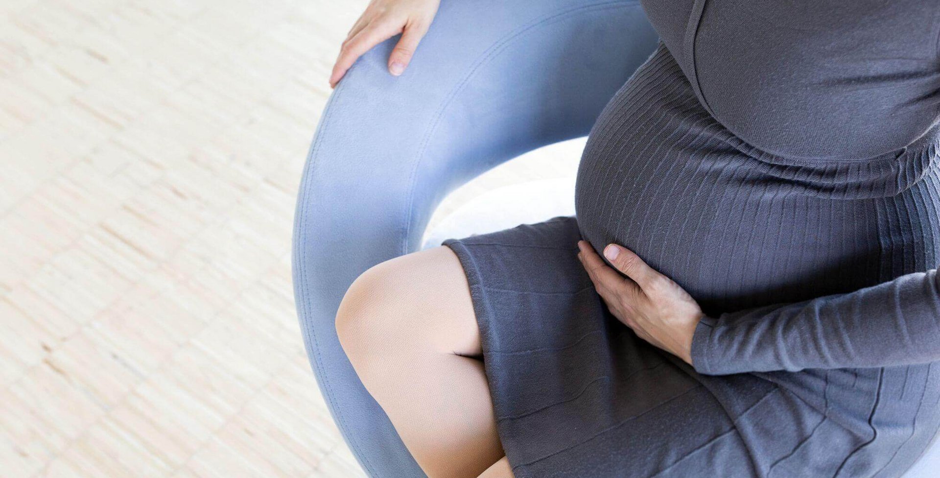 Een zwangere vrouw zit op een stoel en streelt met haar linkerhand over haar babybuik. Vooral zwangere vrouwen krijgen vaak te maken met bekkeninstabiliteit door de enorme verandering en belasting van het lichaam.