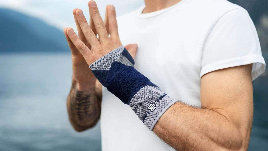 Bijgesneden beeld van een man bij een meer die een yogahouding aanneemt en daarbij een ManuTrain polsbandage draagt om pijn in de pols te verlichten.