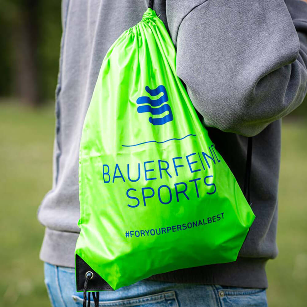 Een persoon draagt een groene Bauerfeind Sports gymtas op de schouder buiten.