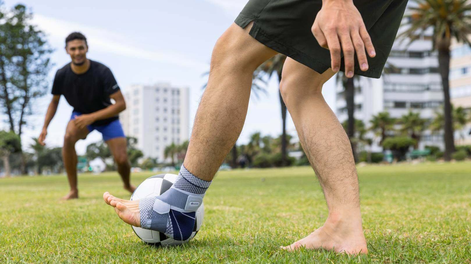 Uitsnede van twee mannen die in het park voetballen. Een van de mannen draagt ter ondersteuning van zijn enkel een MalleoTrain bandage om zijn linkerbeen.