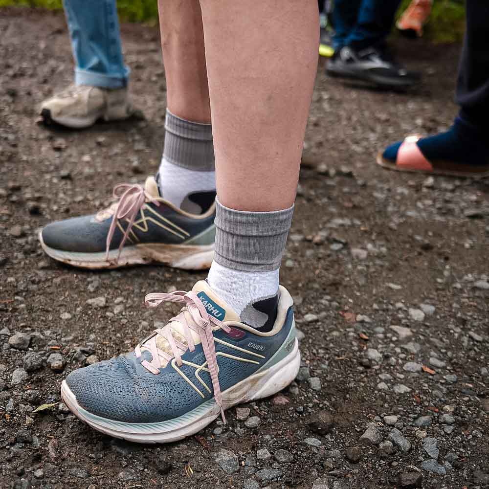 De benen en schoenen van een vrouw die de Bauerfeind Trail Run Mid Cut Socks draagt