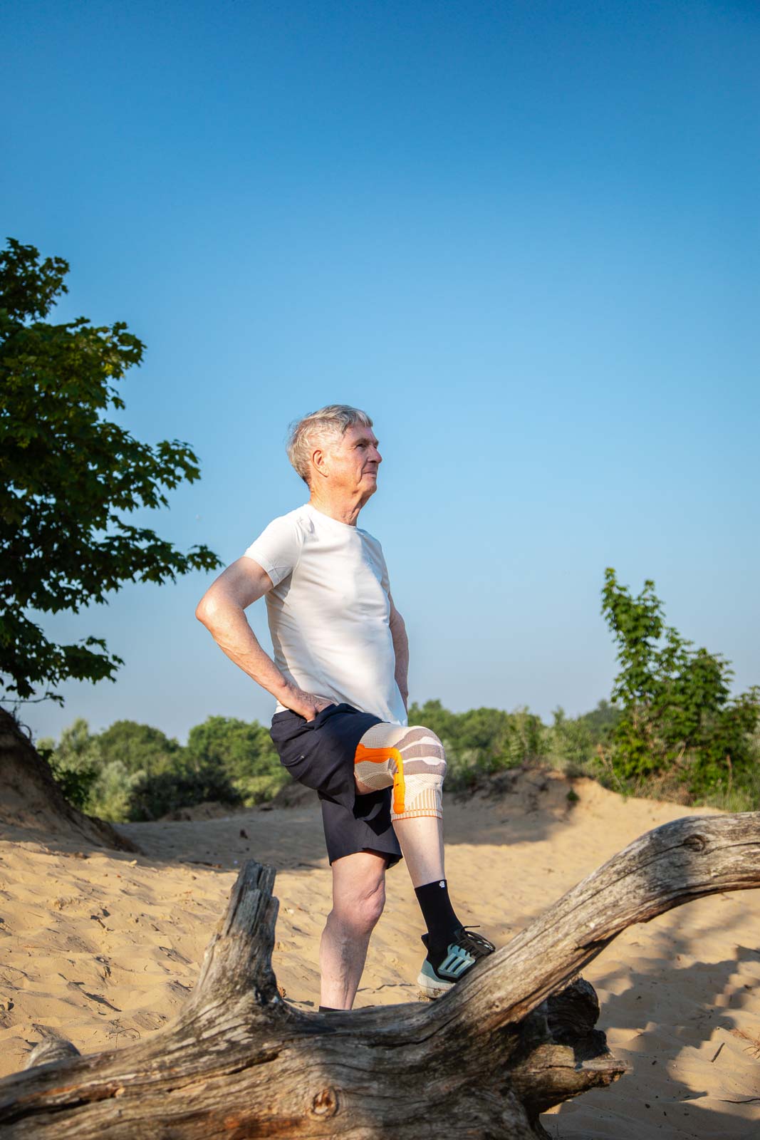 Oudere man met kniebrace staat in de duinen en krijgt steun tijdens een actieve wandeling.