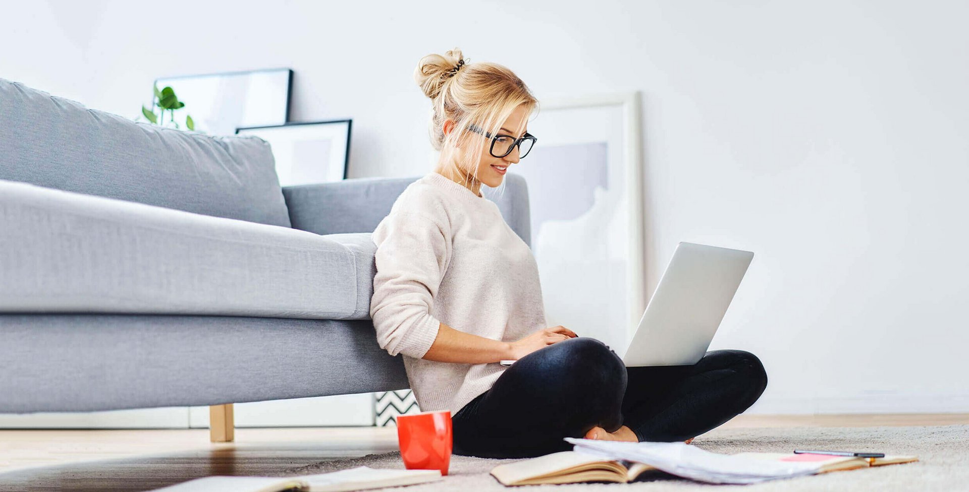 De afbeelding toont een jonge vrouw die met haar laptop op de vloer van haar woning zit te werken.
