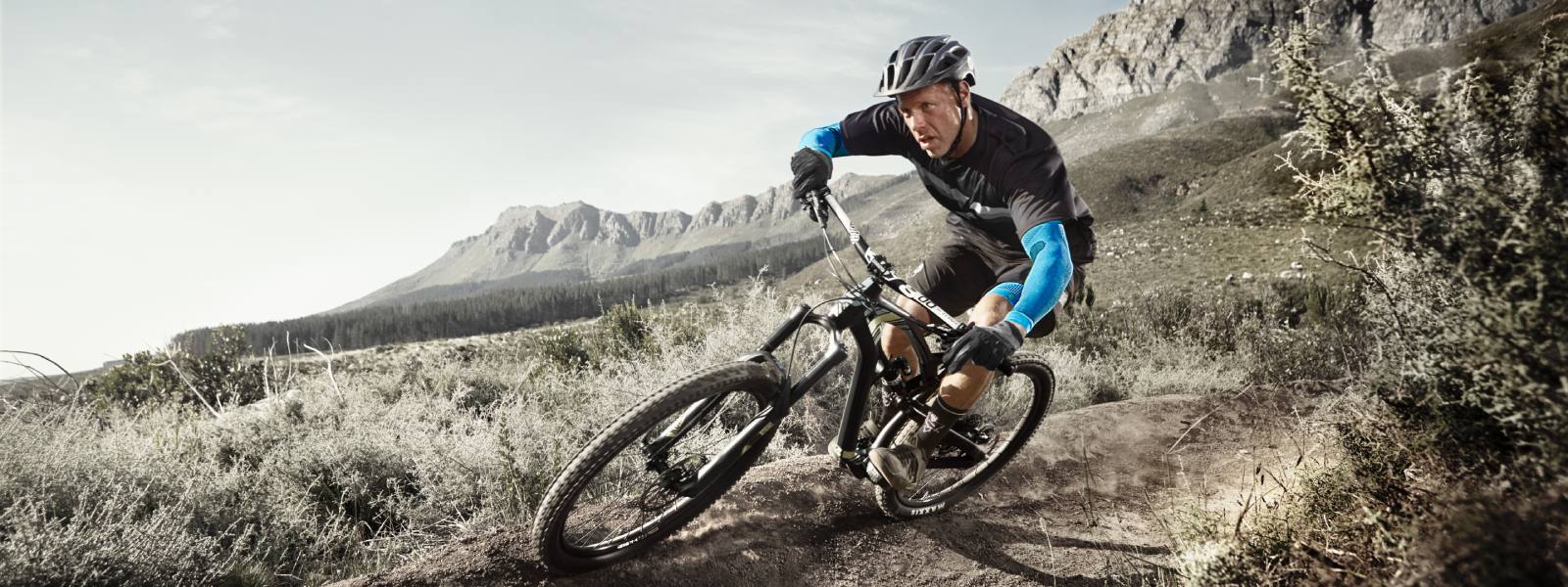 Mountainbiker drijft een helling af en draagt ​​blauwe armmouwen