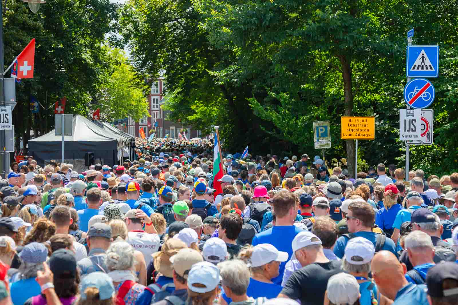 Grote menigte wandelaars tijdens de 4Daagse in Nijmegen, door de straten met vlaggen, borden en zomerse sfeer.