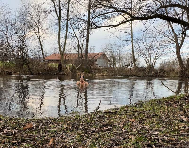 Anna Hahner bidt met gevouwen handen in de rivier, omringd door kale bomen.