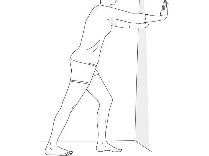 Illustratie van een oefening bij hielpijn: in uitvalspas tegen een muur steunen, het pijnlijke been gestrekt naar achteren met de hiel op de vloer, het voorste been licht gebogen, tot een rek in het achterste been voelbaar is.