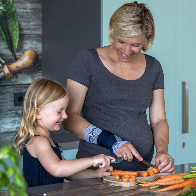 Vrouw draagt titan Bauerfeind ManuTrain polsbrace tijdens koken met haar dochter.