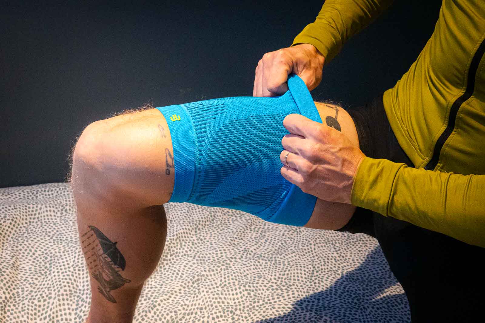 Een fietser in fietskleding trekt een blauwe compressiemouw over zijn bovenbeen