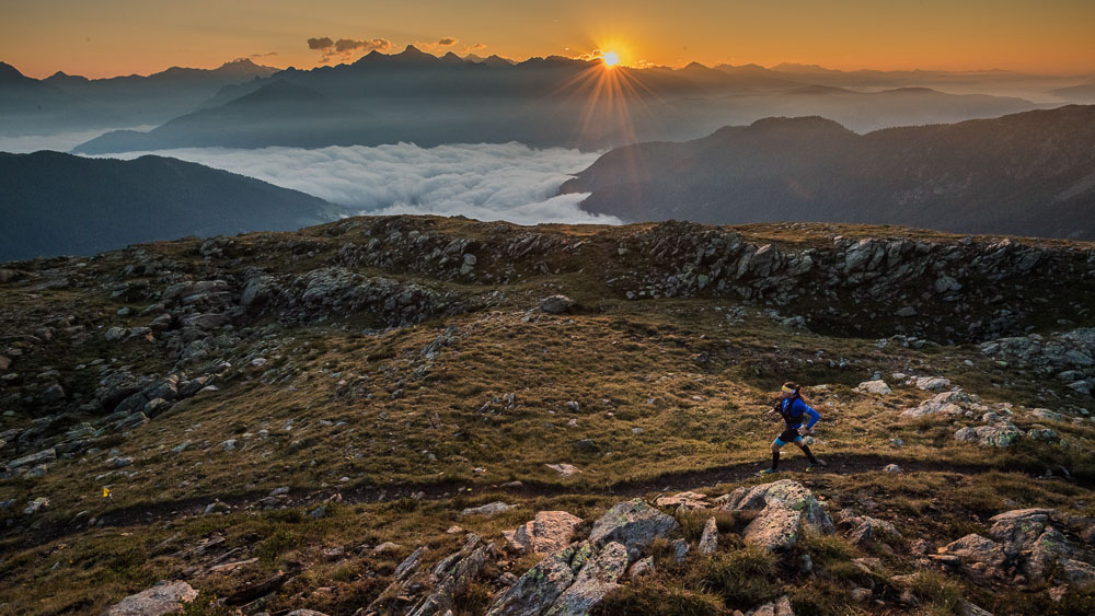 Ultraloper op een bergtrail bij zonsopgang met uitzicht over de Alpen