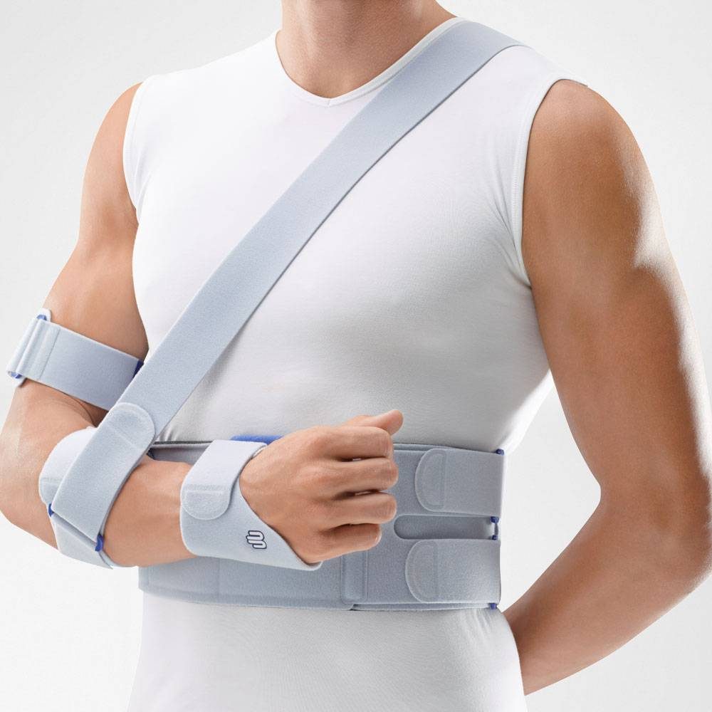 Persoon draagt een grijze schouderbrace met armsteun over een wit mouwloos shirt.