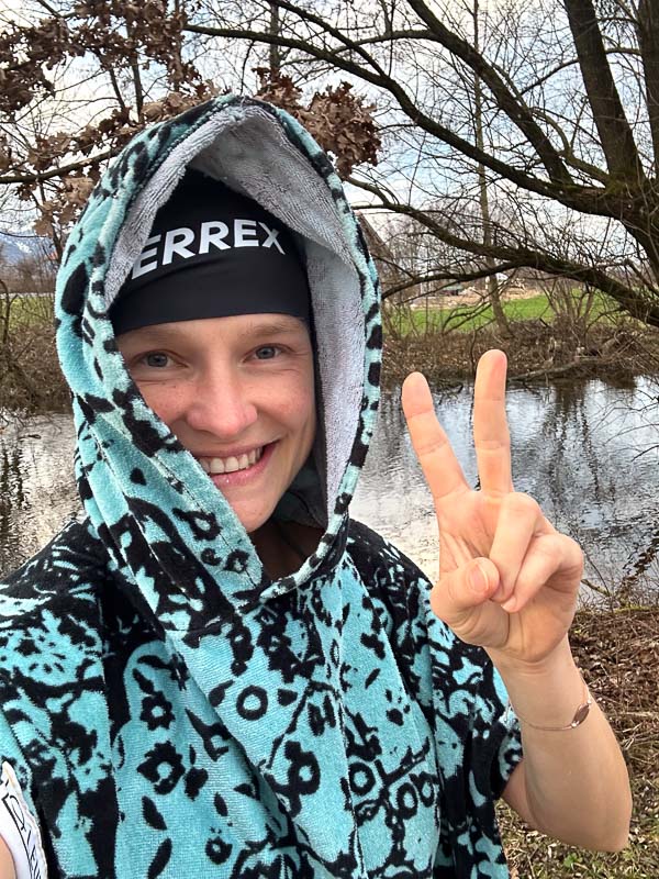 Anna Hahner in een Terrex-muts en kleurrijke poncho, handdoek om haar schouders gewikkeld, toont het vredesteken.