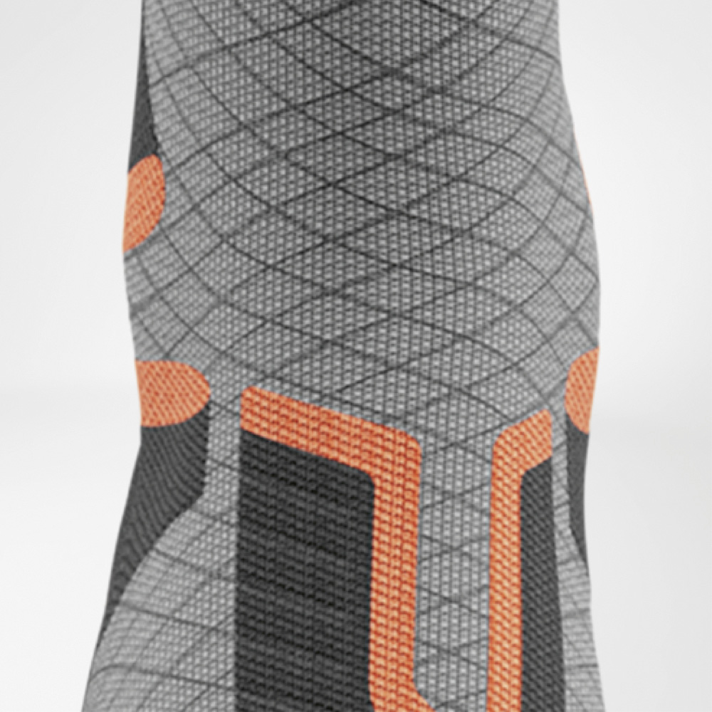 Close-up aan de voorkant van het scheenbeengedeelte van de ski-compressiekous met oranje U-vormige padding en ruitvormige structuur.