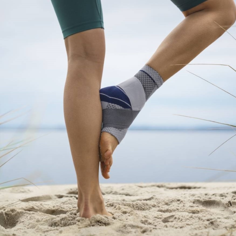 Close-up van persoon die stretcht op strand met grijs-blauwe MalleoTrain Plus enkelbrace.