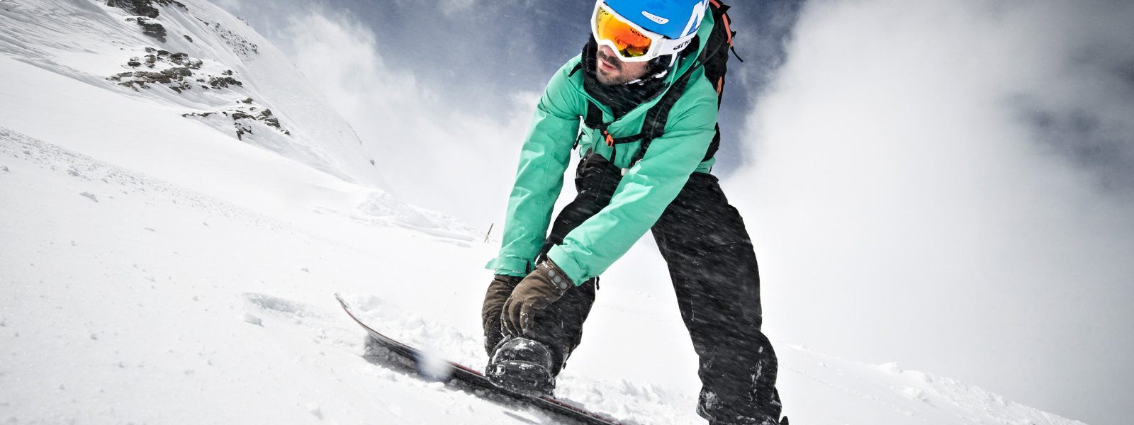 Lichtkikkerperspectief: snowboarders in een groen jasje bevestigd met zijn handen een band en kijkt naar beneden terwijl er veel sneeuw eromheen wordt gericht