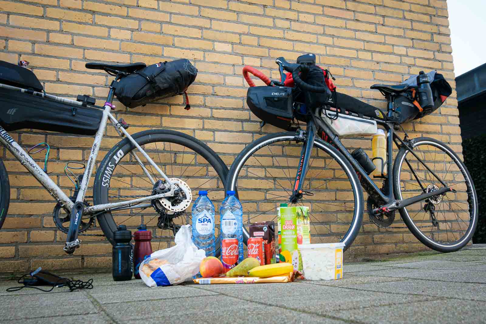 Op de vloer liggen proviand van twee deelnemers aan de Race om Nederland, waaronder water, chocolademelk, aardappelsalade en cola.