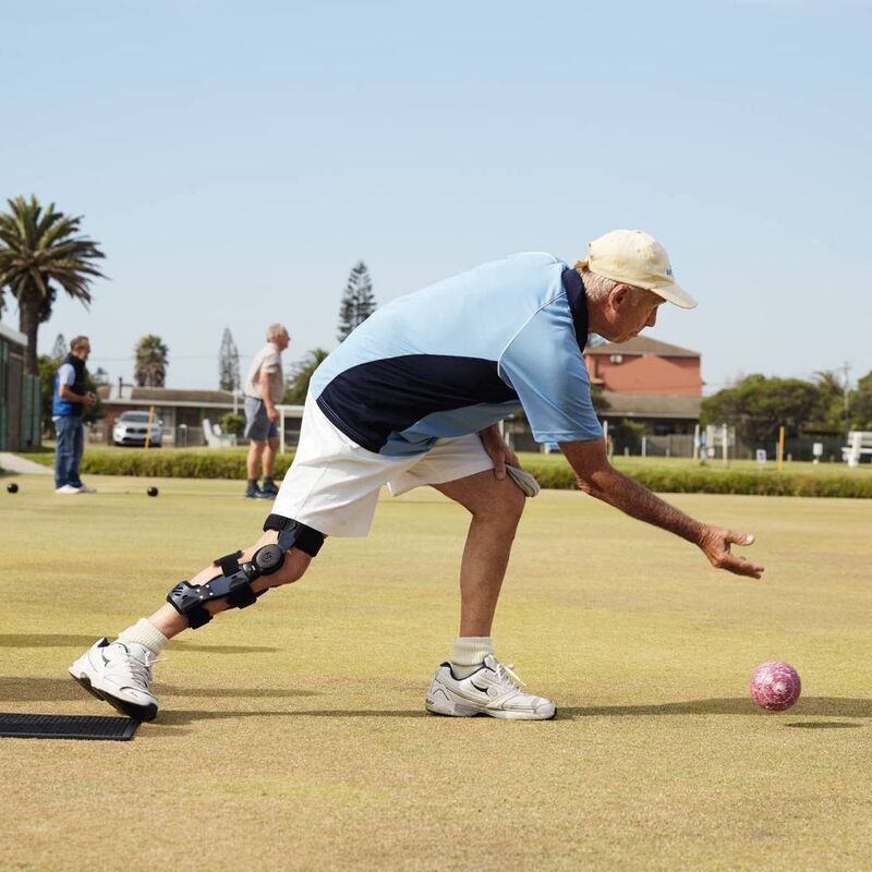 Senior man speelt bowls op zonnige dag met kniebrace voor ondersteuning.