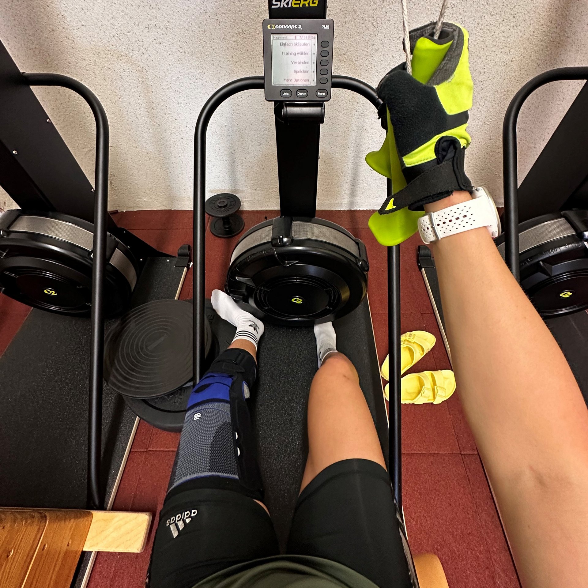 Antonia Horn tijdens haar revalidatiesessie op een SkiErg-trainingstoestel. Ze draagt een SofTec Genu-knieorthese om haar rechterknie en houdt de grepen van het toestel vast met een trainingshandschoen aan haar hand.