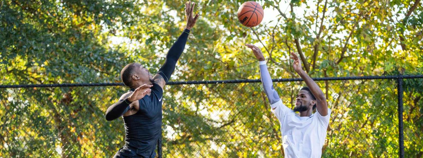 Basketbalspelers in Black Game Clothing proberen zijn tegenstander te blokkeren in witte kleding hoog boven de grond