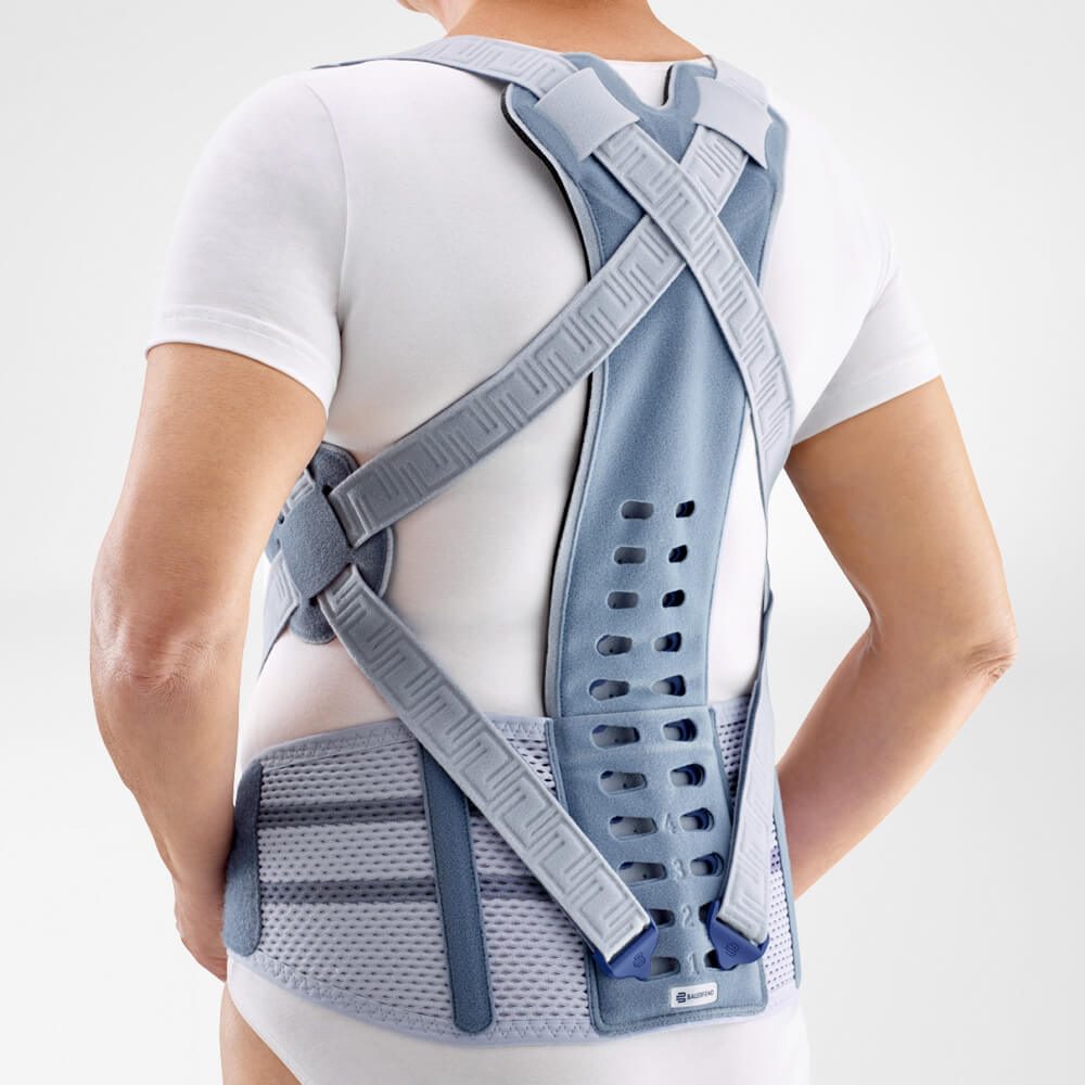 Rugaanzicht van persoon met grijze rugbrace met gekruiste schouderbanden over een wit shirt.