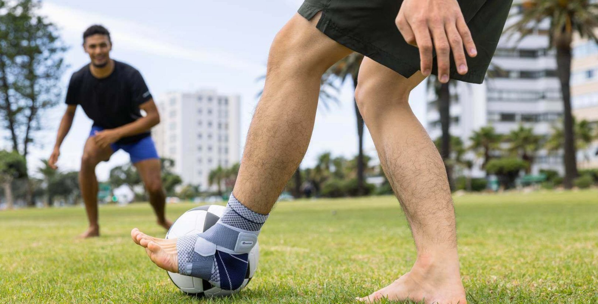 Uitsnede van twee mannen die in het park voetballen. Een van de mannen draagt ter ondersteuning van zijn enkel een MalleoTrain bandage om zijn linkerbeen.