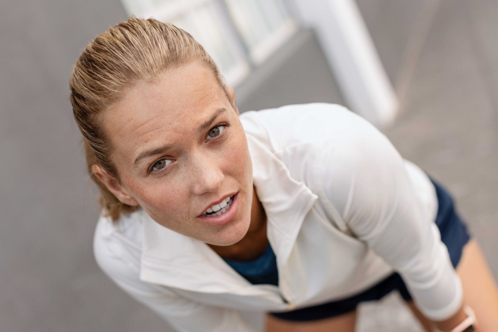 Blonde vrouw met een witte sporttrui kijkt rechtstreeks in de camera
