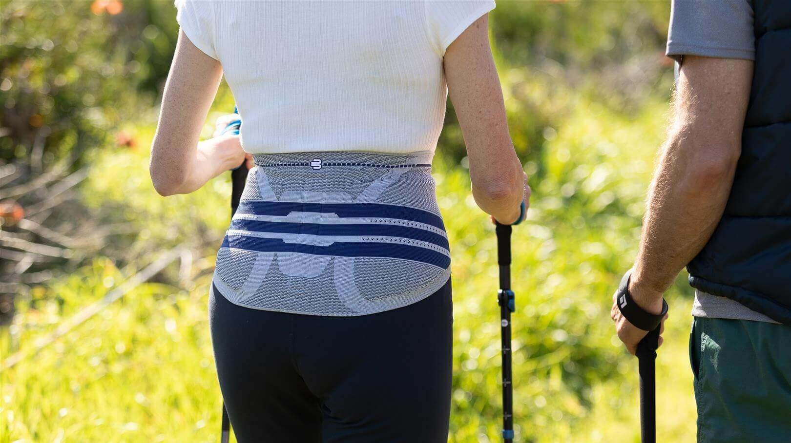 Detailopname van een vrouw tijdens het nordic walking in de natuur, die ter ontlasting van haar rug een LumboTrain bandage draagt.
