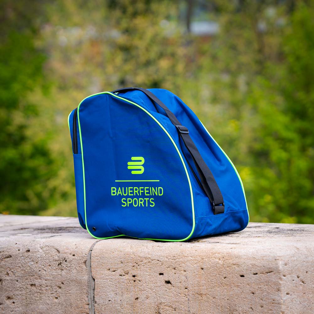 Een blauwe tas met het Bauerfeind Sports logo, gefotografeerd buiten op een stenen achtergrond. De tas heeft groene accenten en zwarte riemen.