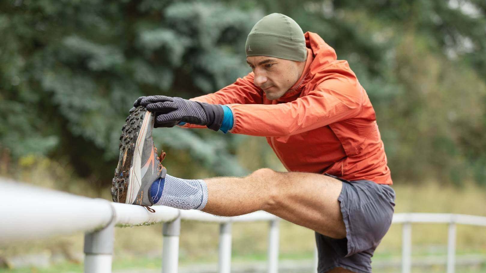 Man in sportkleding rekt zijn been op een reling en draagt een AchilloTrain bandage aan zijn linkerenkel.
