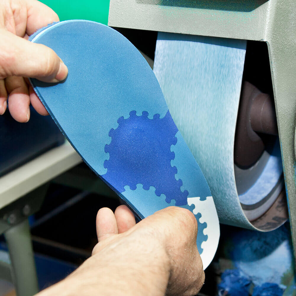 Een medewerker schuurt een TRIactive van Bauerfeind, een orthopedische inlegzool met aan de belasting aangepaste zones.