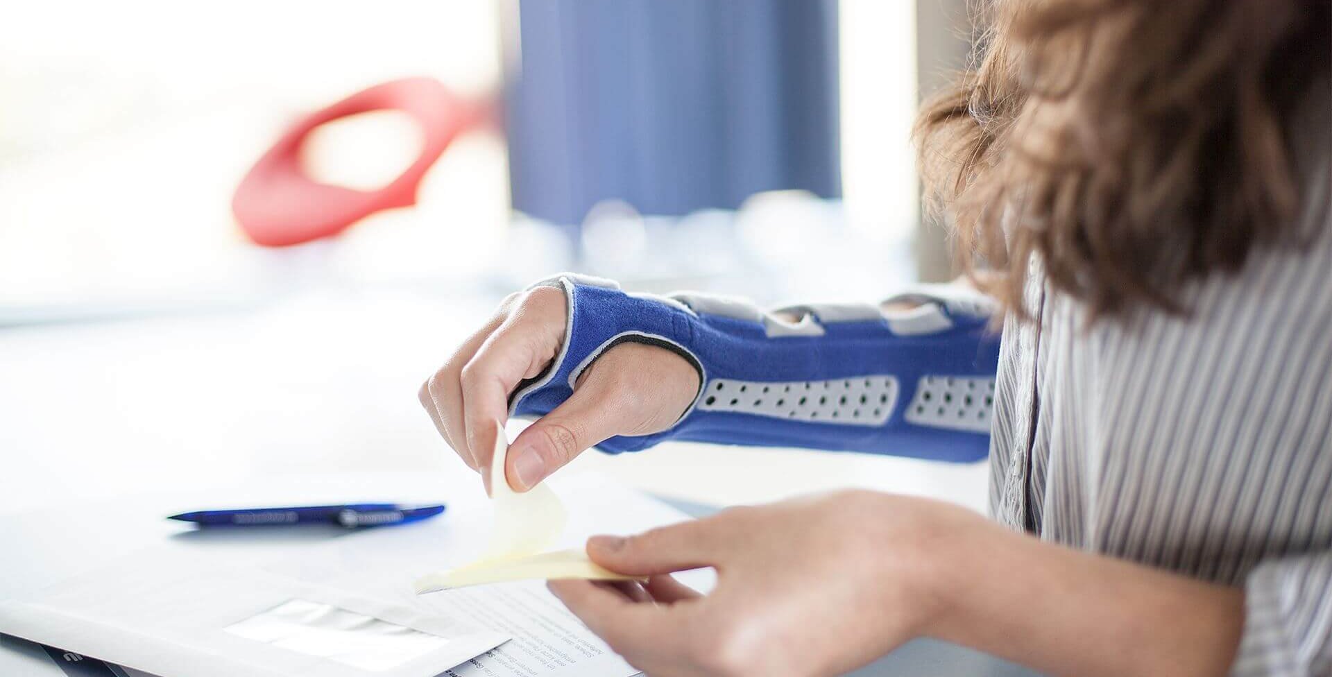 Beelduitsnede van een vrouw tijdens het werken aan haar bureau. Ze draagt een ManuLoc Long, een stabiliserende polsbandage van Bauerfeind, die onder andere bij een carpaletunnelsyndroom wordt gebruikt.