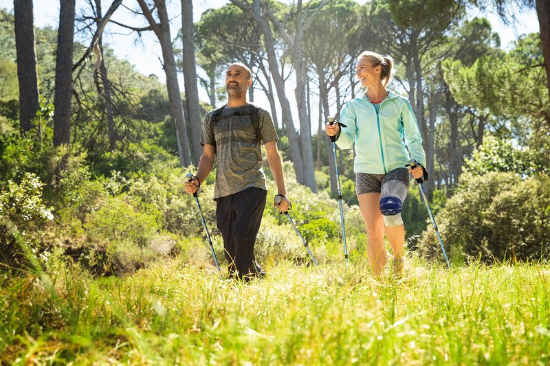 De foto toont een paar tijdens het nordic walking. De vrouw draagt een GenuTrain A3 kniebandage van Bauerfeind tegen artrosegerelateerde pijn.